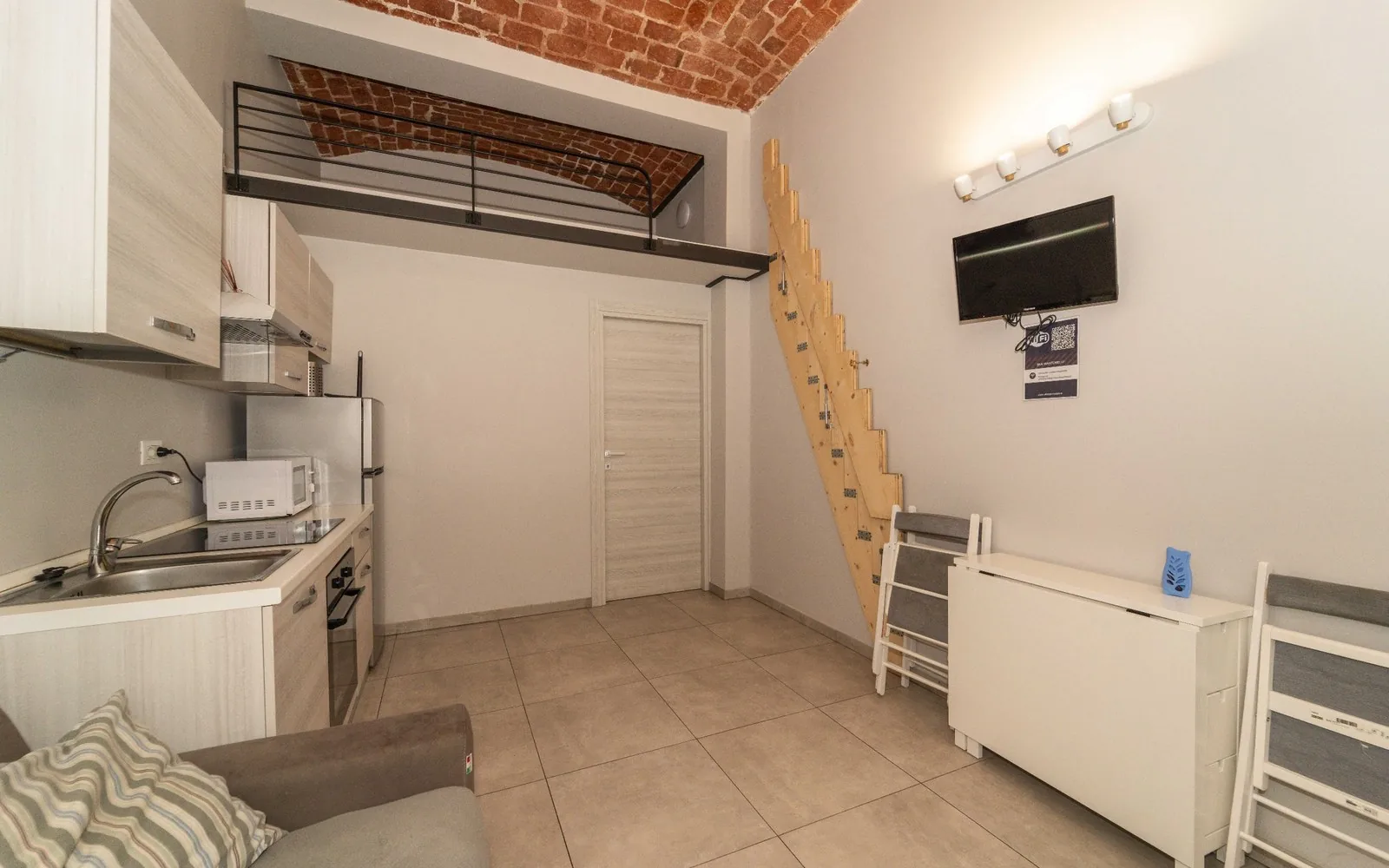 Zona giorno con TV, cucina e scala del soppalco in un bilocale COBER IMMOBILIARE a Torino